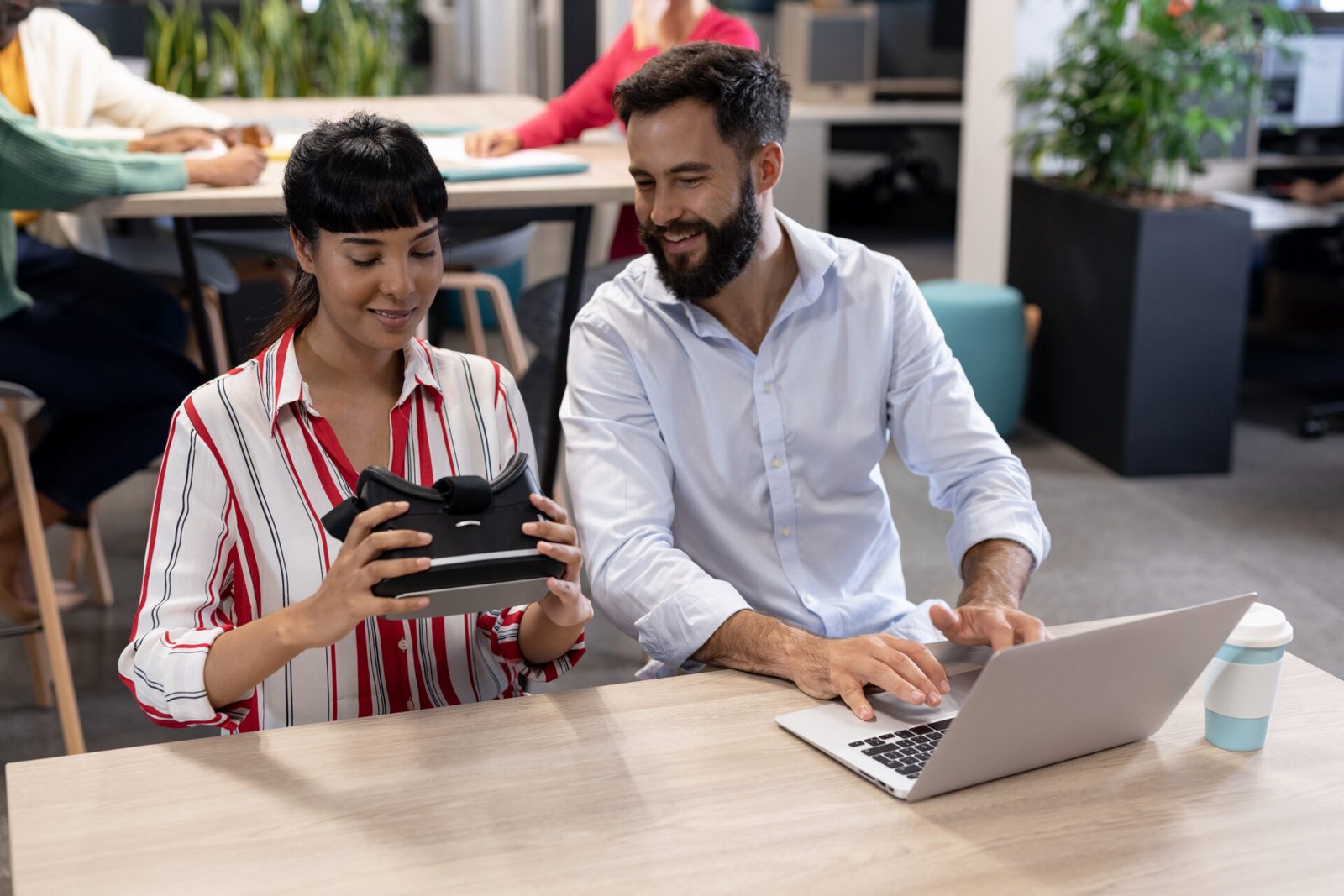 smiling-biracial-business-colleagues-discussing-over-vr-simulator-with-laptop-during-meeting-unaltered-business-teamwork-modern-office-and-technology-concept