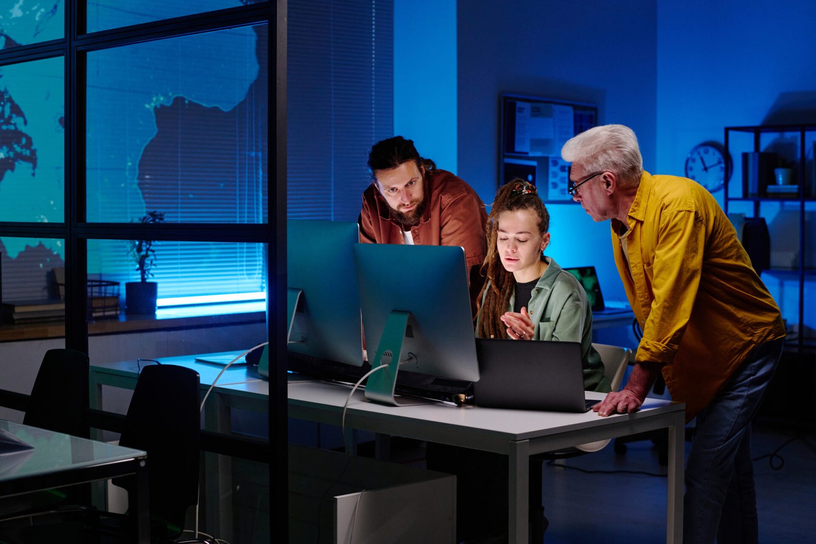 three-colleagues-working-over-new-project-or-software-in-front-of-desktop-computers-while-young-woman-explaining-something-to-men